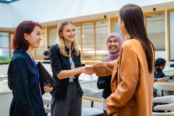 Group of professional women—including a woman in hijab—smiling and shaking hands in a business setting