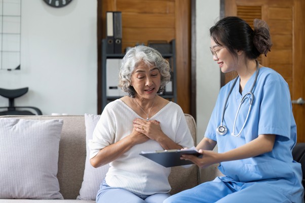Smiling nurse in scrubs showing information to an elderly woman during a home health consultation on a sofa