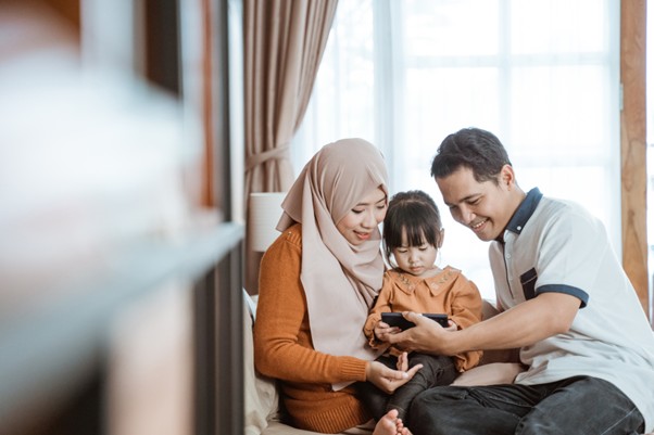 Young Malaysian Muslim family sitting together at home, smiling and bonding — symbolising the care and security provided by Group Takaful employee benefits