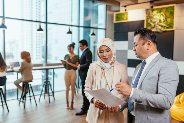 Businesswoman in a printed hijab reviewing documents with a colleague in a modern office with city views