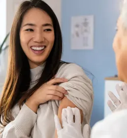 Smiling woman at a clinic receiving a vaccination from a medical professional