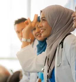Smiling Muslim female doctor in hijab raising her hand during a medical workshop with colleagues