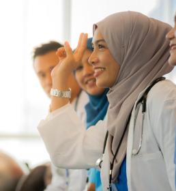 Smiling Muslim female doctor in hijab raising her hand during a medical workshop with colleagues