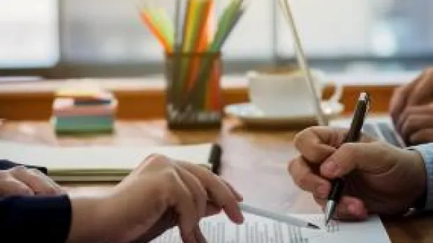 Two people sat at a desk reviewing a document Two people sat at a desk reviewing a document