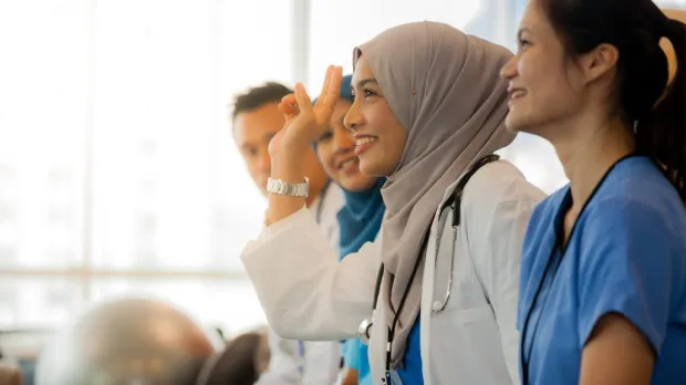Female Muslim doctor raising hand during medical seminar Smiling Muslim female doctor in hijab raising her hand during a medical workshop with colleagues