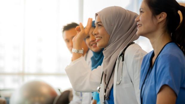 Smiling Muslim female doctor in hijab raising her hand during a medical workshop with colleagues