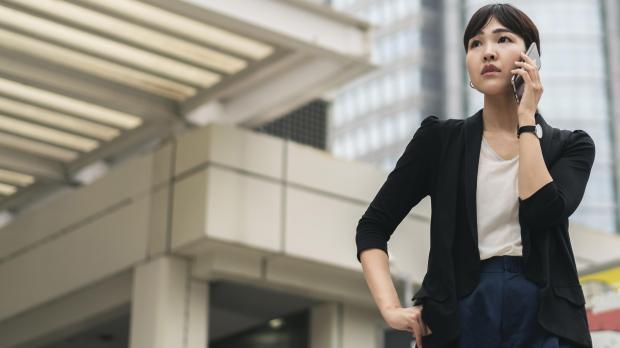 Asian businesswoman in smart attire speaking on the phone while standing outside a commercial building in an urban setting