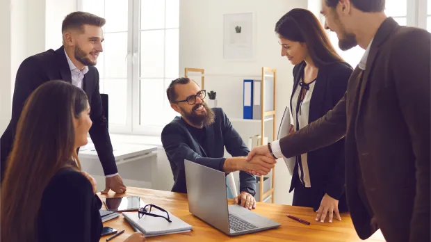 Smiling Business Partners Shaking Hands after Successful Negotiations with Colleagues in Office