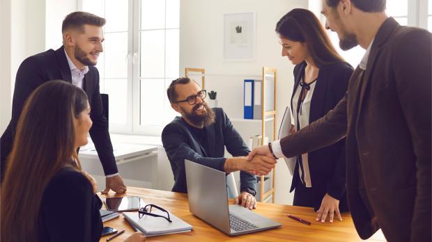Smiling Business Partners Shaking Hands after Successful Negotiations with Colleagues in Office