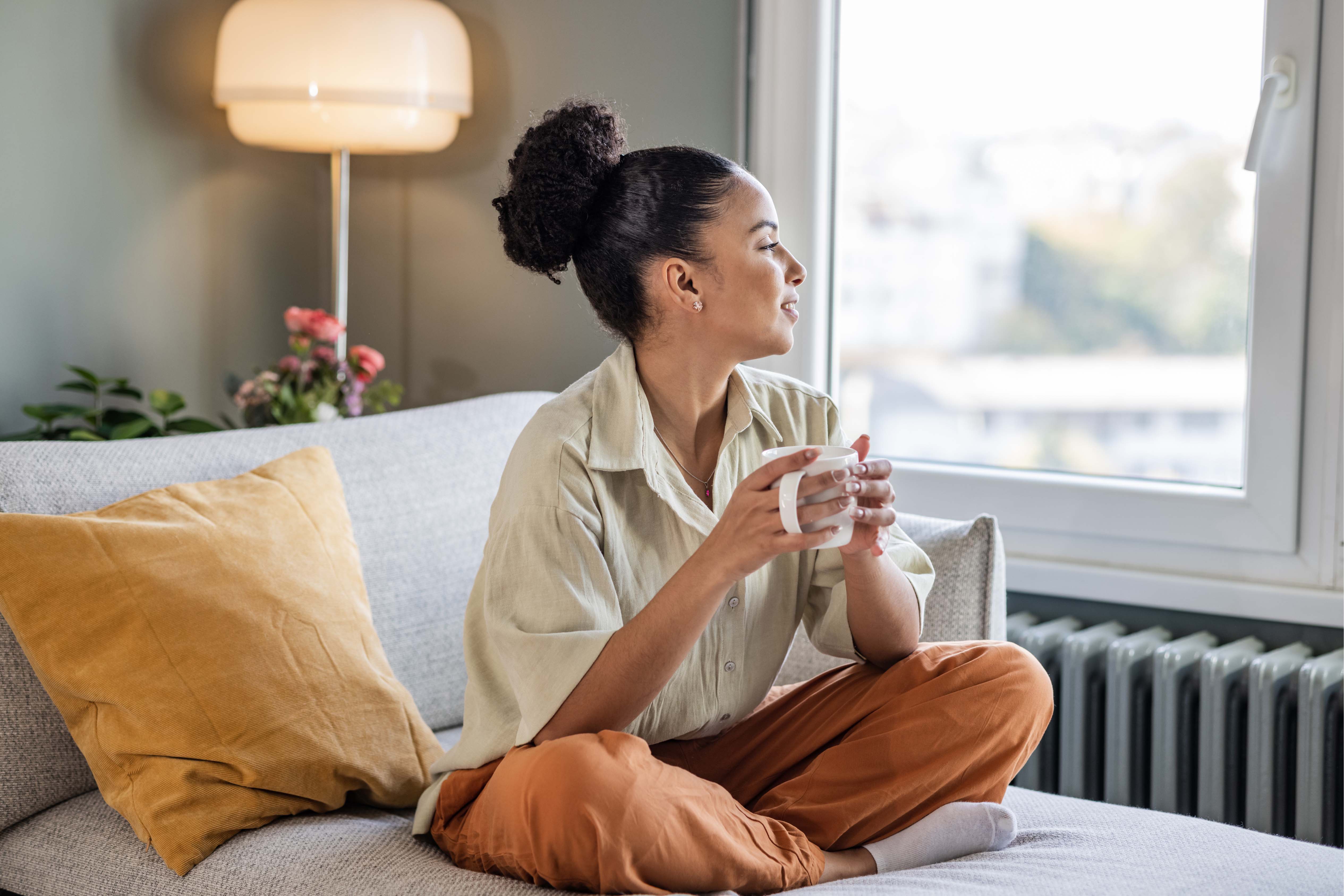 Tranquillity and wellbeing. Female sitting on bed having a warm beverage