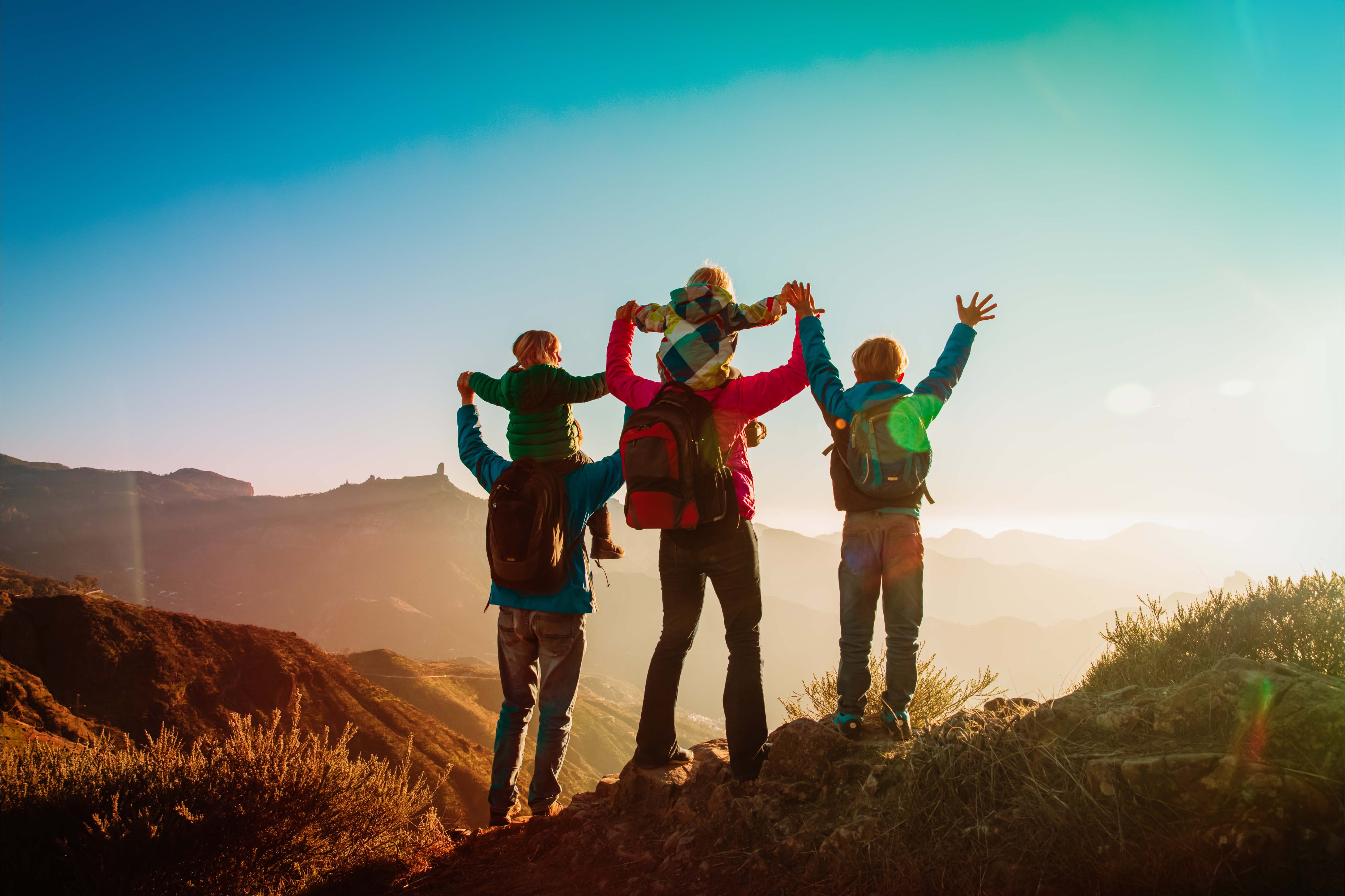 A family with children hiking in the mountains, raising their arms in celebration at the summit during sunrise, symbolizing wellbeing, balance, and shared achievement.