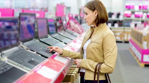 A lady in a tan leather jacket tries out a new laptop in a technology store