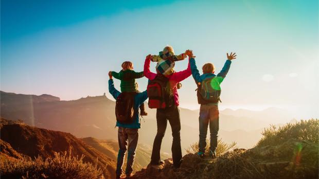 Family celebrating together at mountain summit at sunrise A family with children hiking in the mountains, raising their arms in celebration at the summit during sunrise, symbolizing wellbeing, balance, and shared achievement.