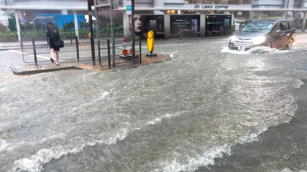 A woman tries to cross a heavily flooded high street as a car drives past in deep water