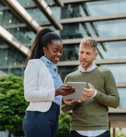 two people outside talking while looking at a tablet