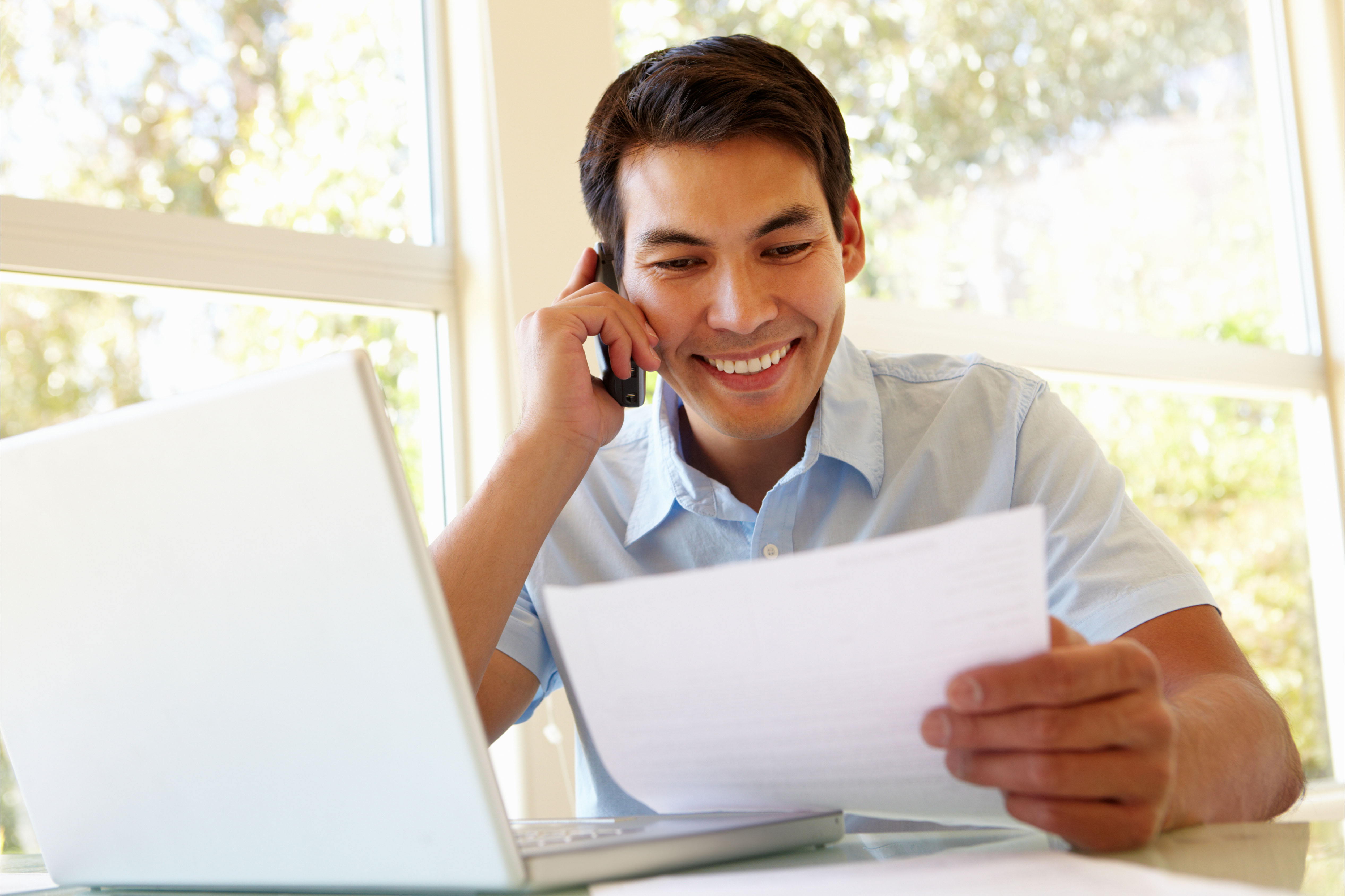 Man reviewing documents while speaking on the phone and working on a laptop, representing support and easy communication for SMEs.