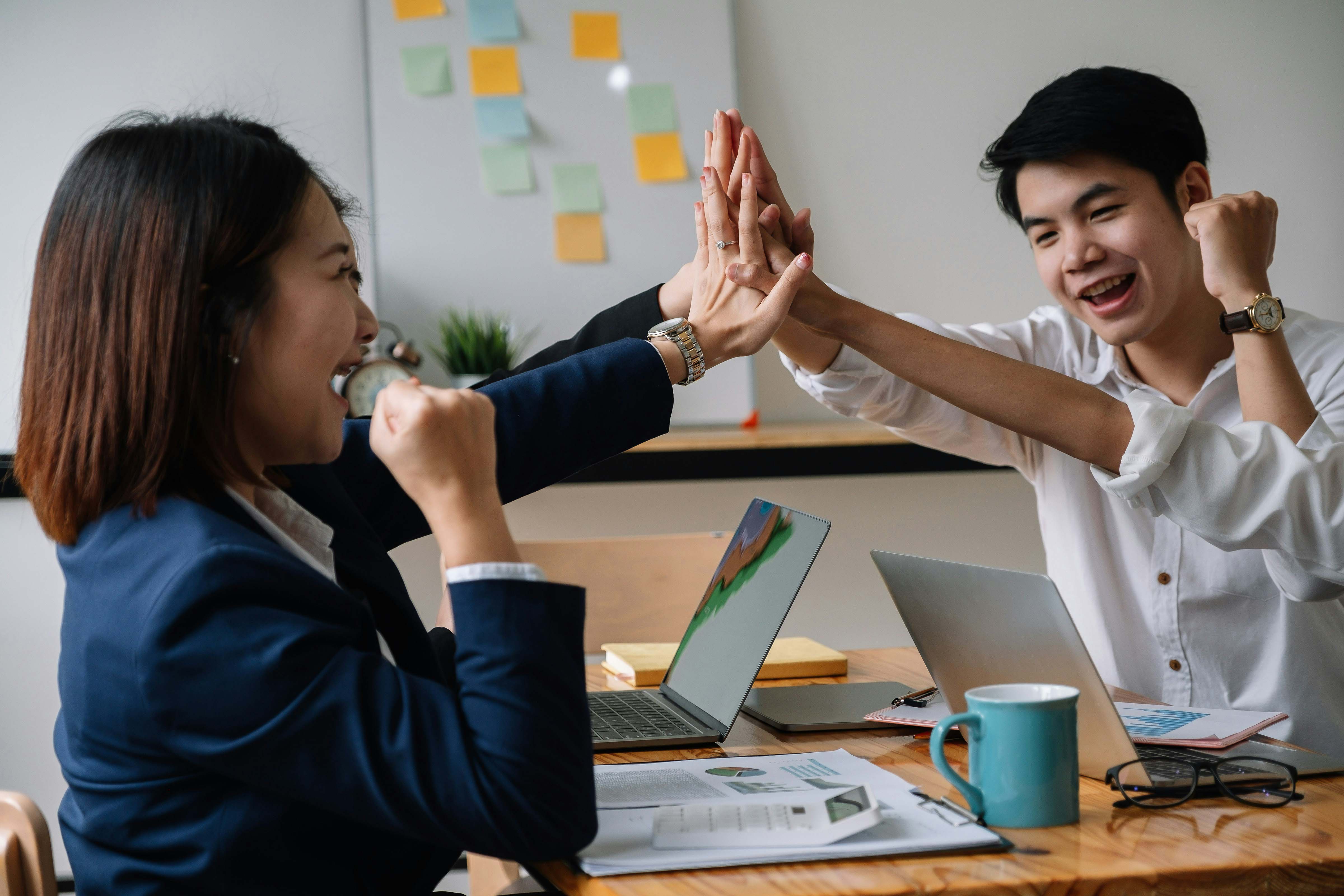 Two coworkers high-fiving across a desk in celebration