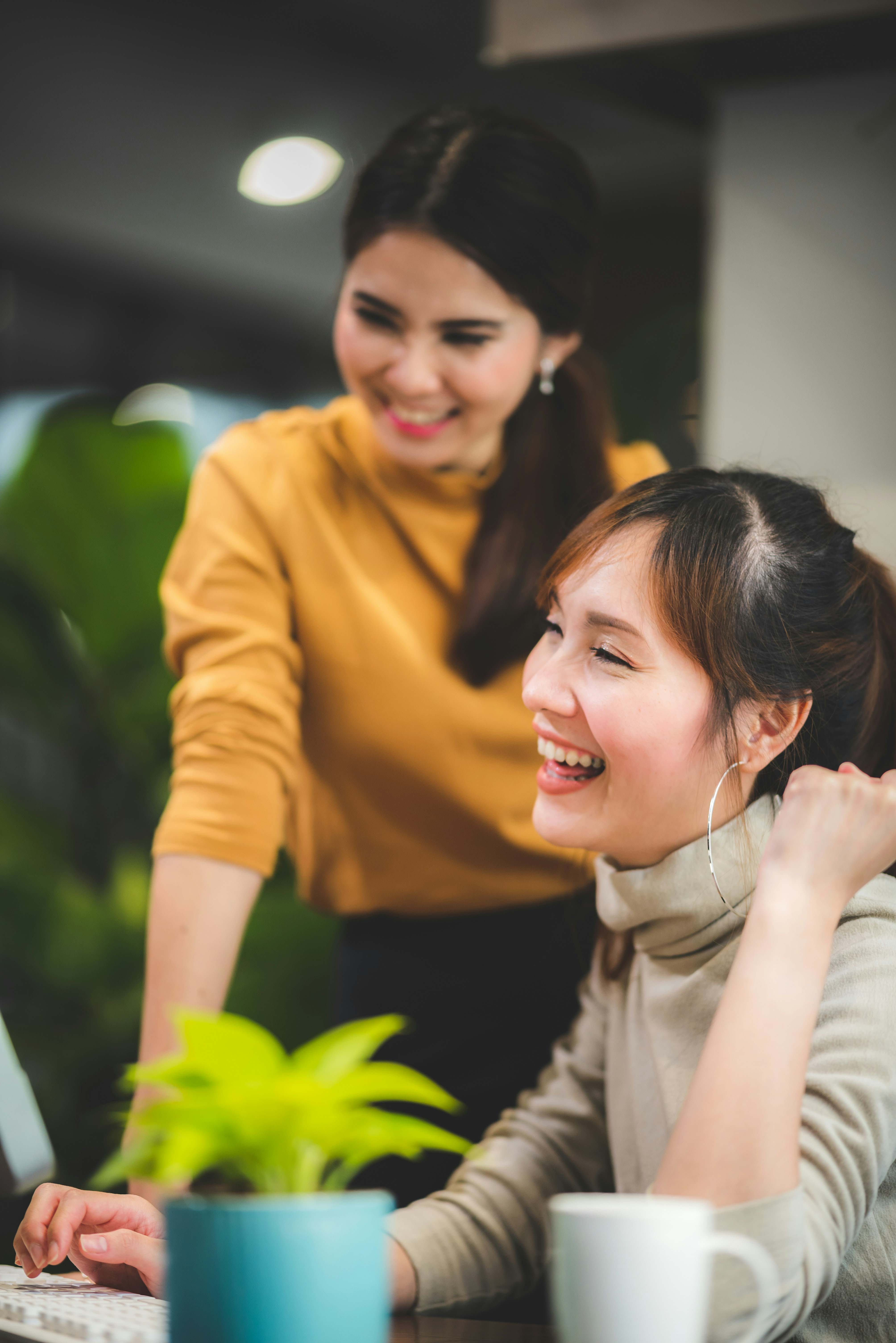 Two female employees smiling and working together in an office setting