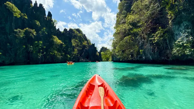Kayaking through turquoise lagoon Red kayak on clear turquoise water between limestone cliffs in the Philippines