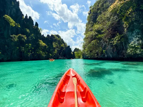 Red kayak on clear turquoise water between limestone cliffs in the Philippines