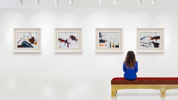 A young woman sits on a bench in a museum admiring the modern art on the wall in front of her
