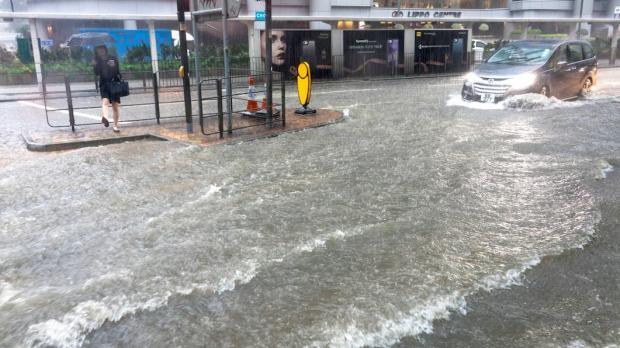 A woman tries to cross a heavily flooded high street as a car drives past in deep water