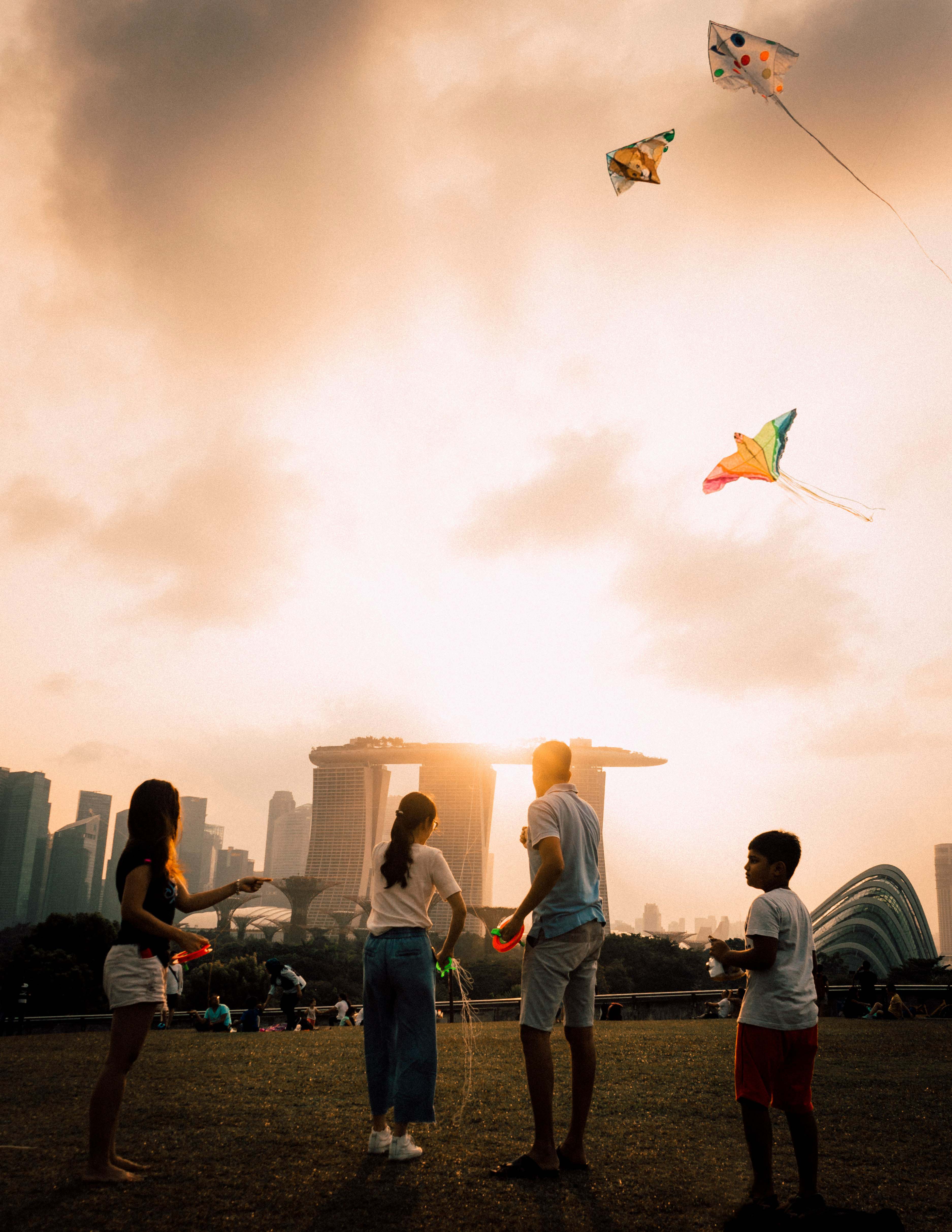 Group of people flying kites at Marina Barrage in Singapore at sunset, with Marina Bay Sands and city skyline in the background.