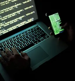 A computer hacker working on a laptop and a smartphone