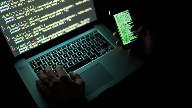 A computer hacker working on a laptop and a smartphone