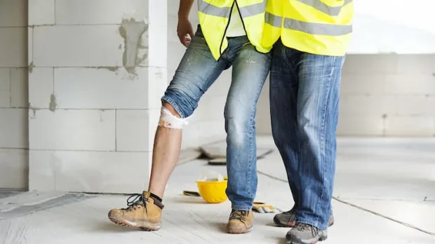 Workmen compensation workman with bandaged knee being supported by collegue