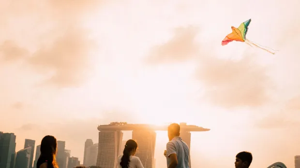 Sunset Kite Flying at Marina Barrage – Family Fun in the Heart of Singapore Group of people flying kites at Marina Barrage in Singapore at sunset, with Marina Bay Sands and city skyline in the background.