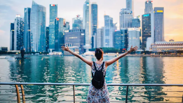 Celebrating Singapore’s Skyline Person with arms raised looking at Singapore’s Marina Bay skyline at sunset, symbolising opportunity and growth