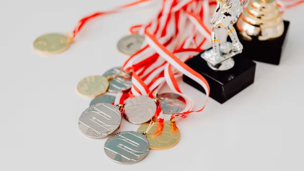 Una colección variada de medallas de plata y oro junto a trofeos sobre una superficie blanca, mostrando logros.