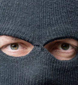 A man in a balaclava looks directly into the camera