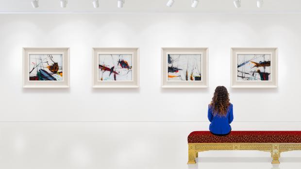 A young woman sits in an art gallery viewing four paintings on the wall