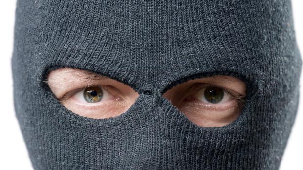 A man in a balaclava looks directly into the camera