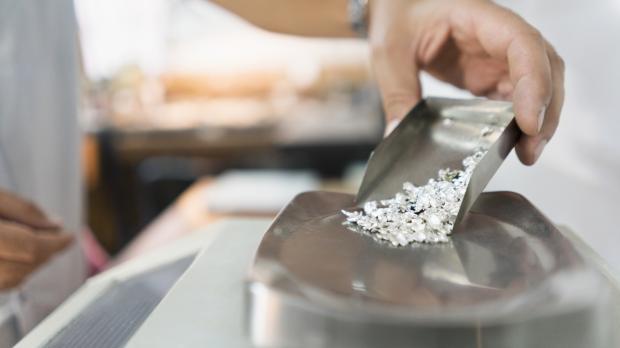 A jeweller pours uncut diamonds onto a scale