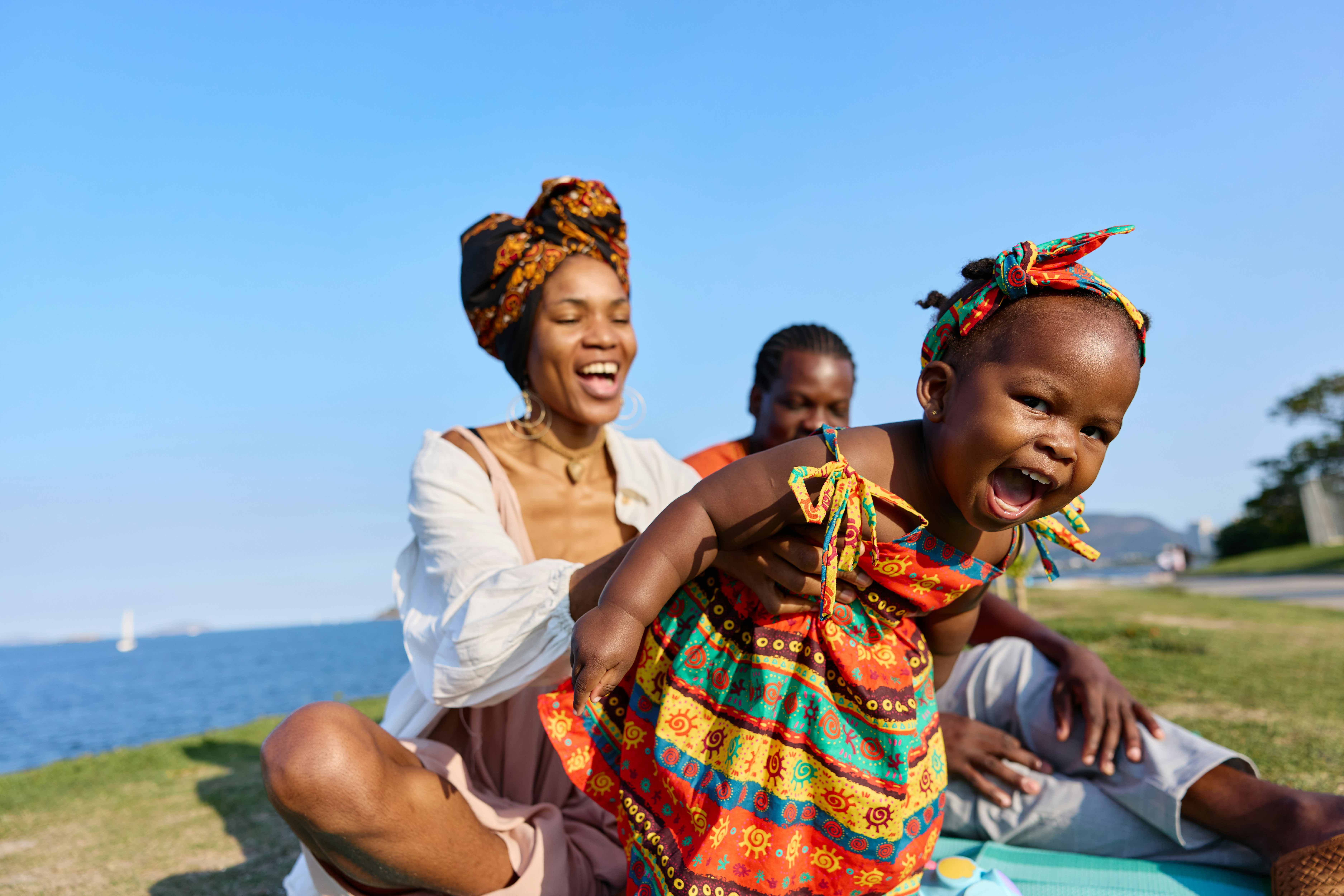 Smiling family enjoying time together outdoors by the water as parents play with their young child.