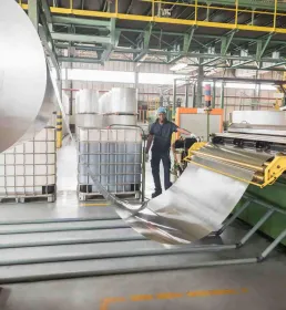 A man stands by a large roller in an aluminium factory
