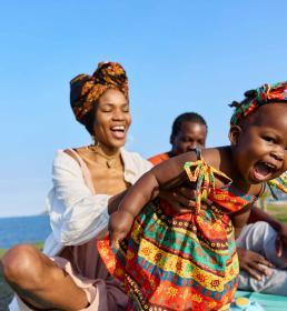 Smiling family enjoying time together outdoors by the water as parents play with their young child.