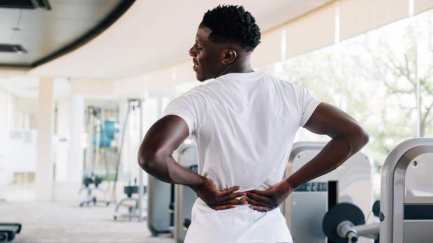 A man in the gym holds his hands to his lower back in pain