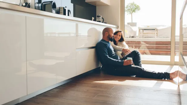 Home and contents - young couple sit on floor of their kitchen A young couple sit on floor of their kitchen, smiling and drinking coffee