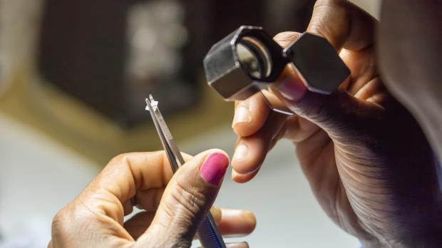 A close-up view of a jeweller holding a diamond between tweezers, and examining it using a magnifying glass