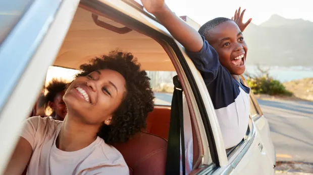 Motor - mum and son in car A mum and son go on a drive. She smiles in the front of the car as he leans out of the back window, arms raised in happiness