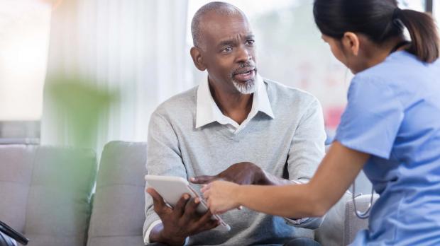 An older patient talks with his doctor. She shows him results on a tablet computer and he looks concerned, asking questions about his diagnosis