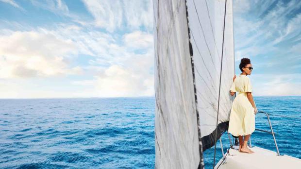 A woman in a summer dress stands on the bow of a private yacht