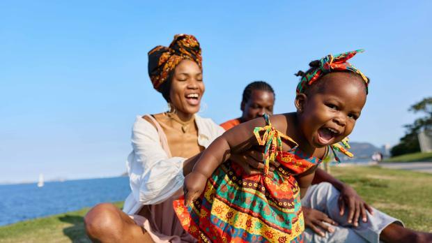 Smiling family enjoying time together outdoors by the water as parents play with their young child.
