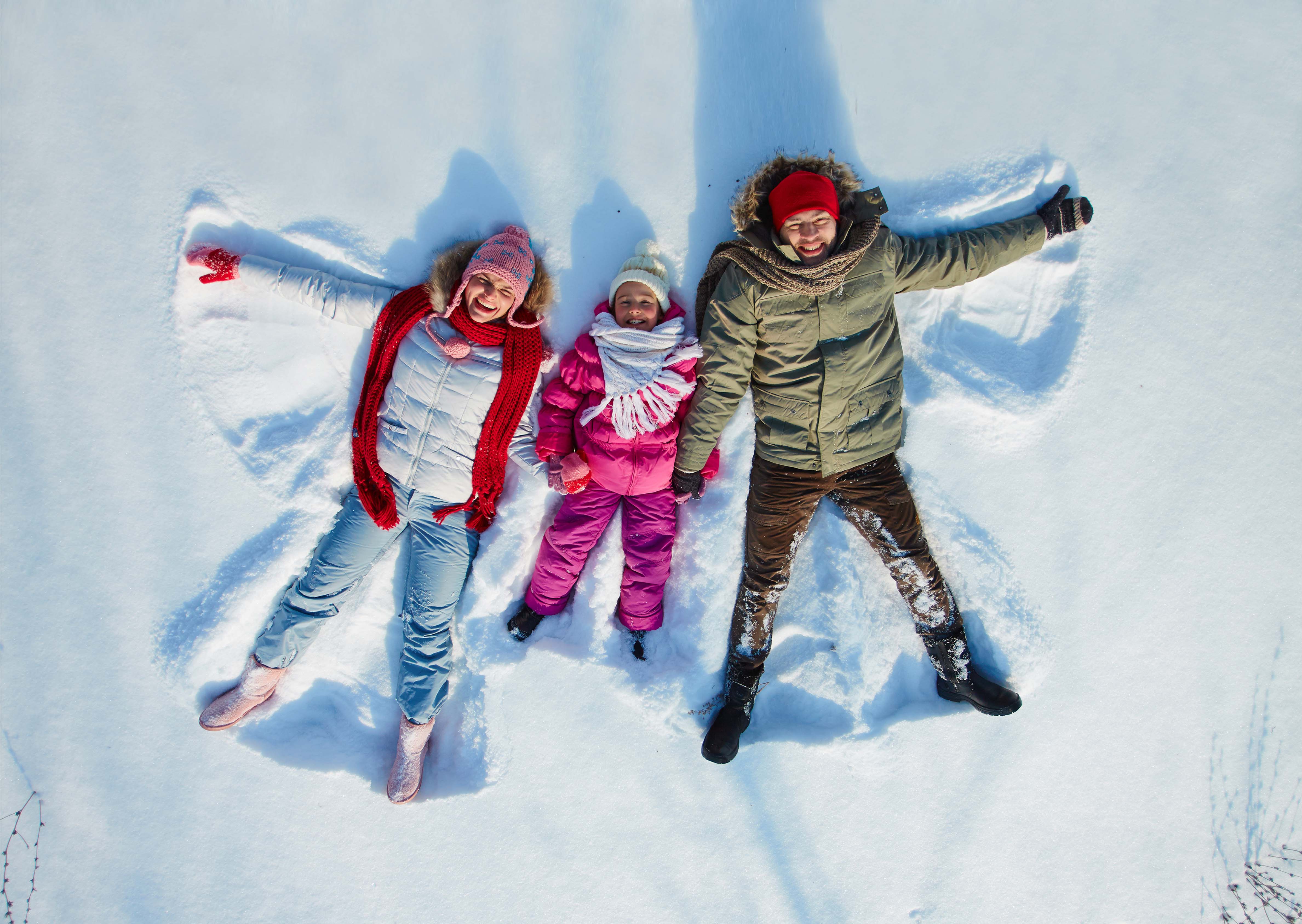 Parents and child lying in the snow making snow angels, symbolising joy, winter fun, and togetherness.