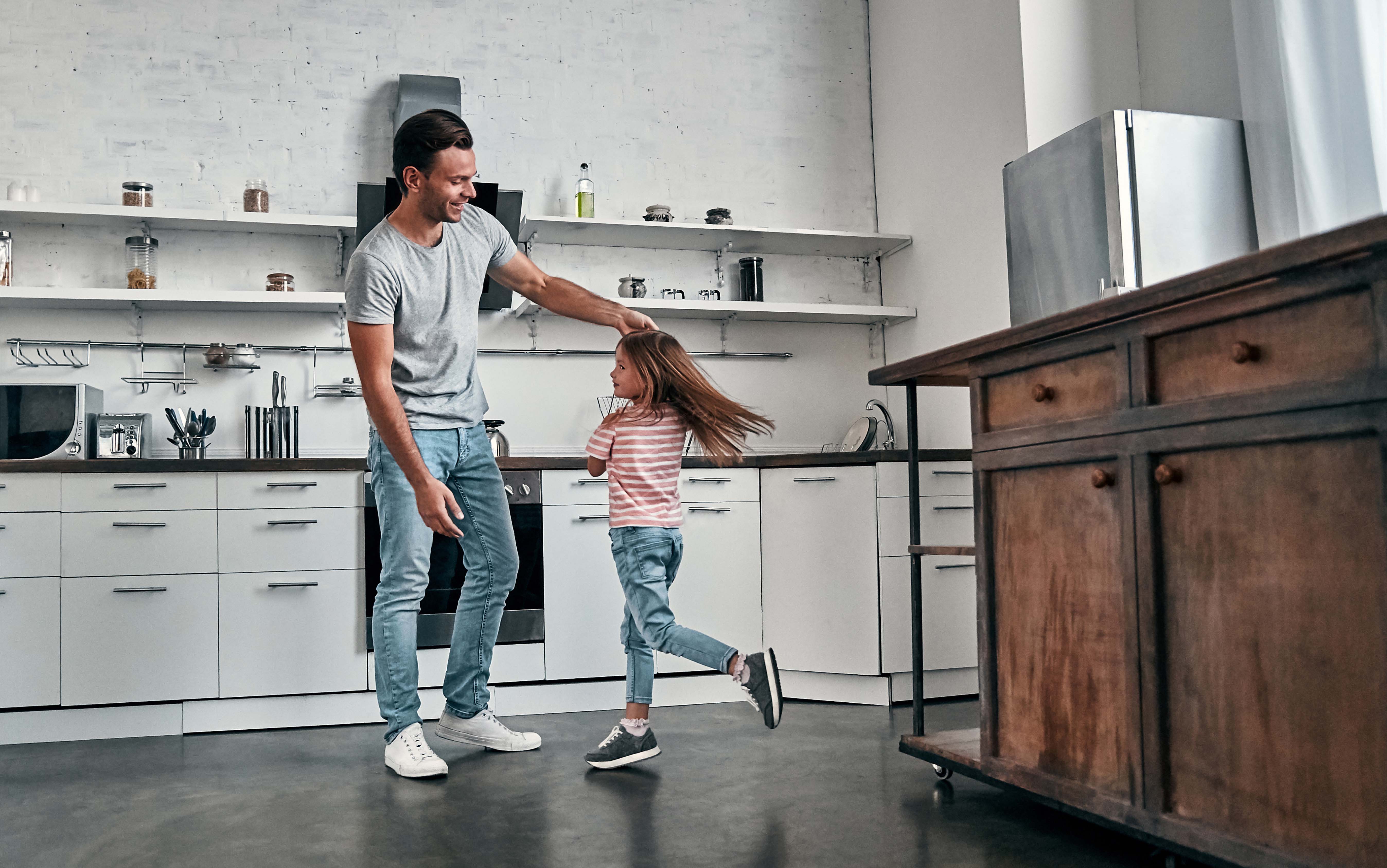 Smiling father and young daughter dancing together in a bright modern kitchen, enjoying quality time at home