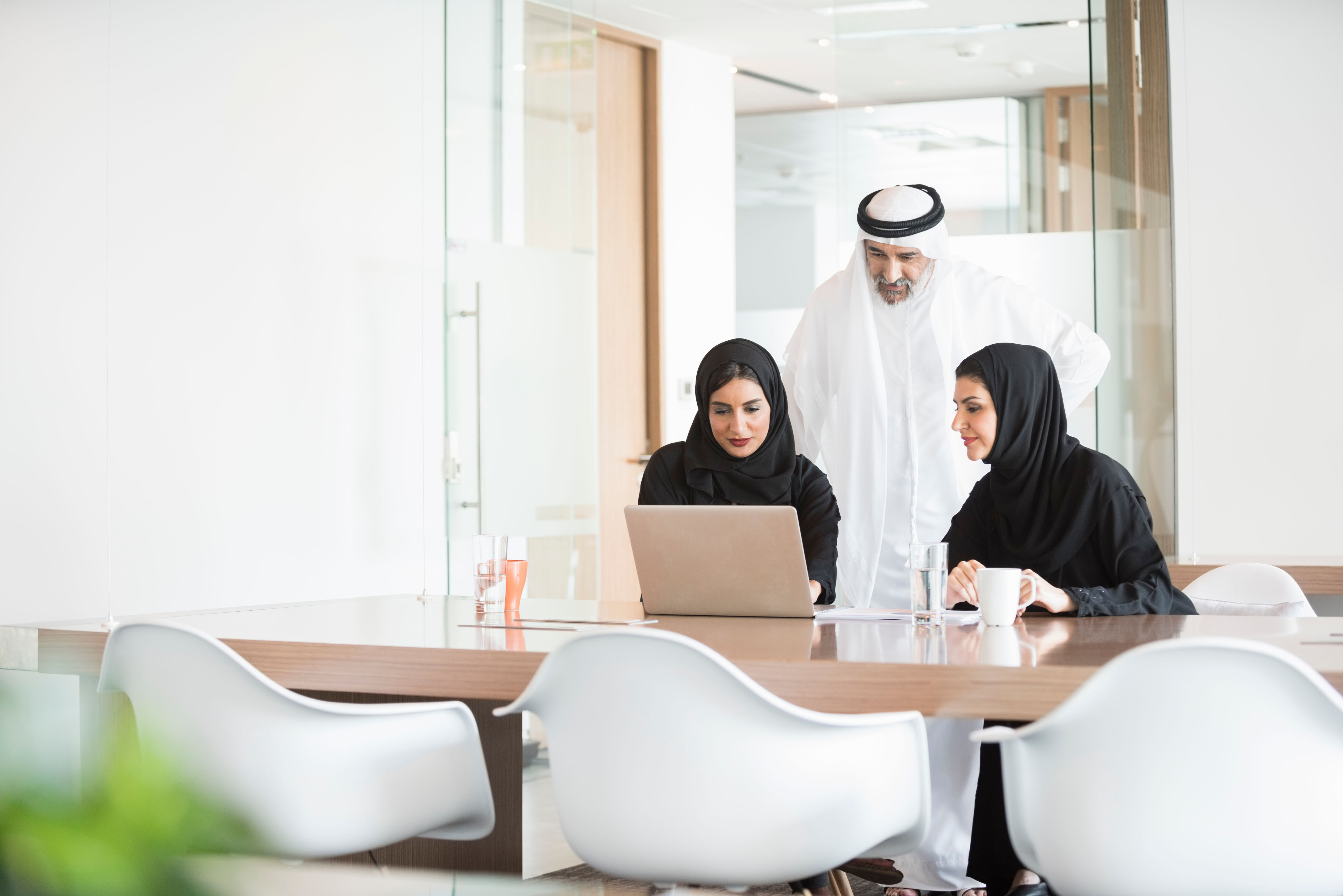 A group of Emirati professionals working together on a laptop in a bright modern office, representing collaboration and tailored employee benefits in the UAE.